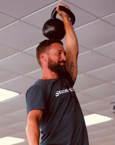 Mike Fickling pressing a kettlebell overhead in the gym
