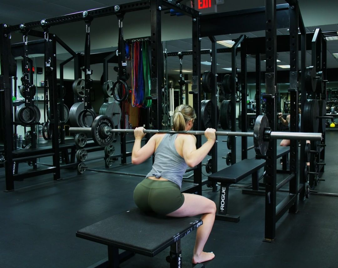 A member box squats with a barbell in the rack.