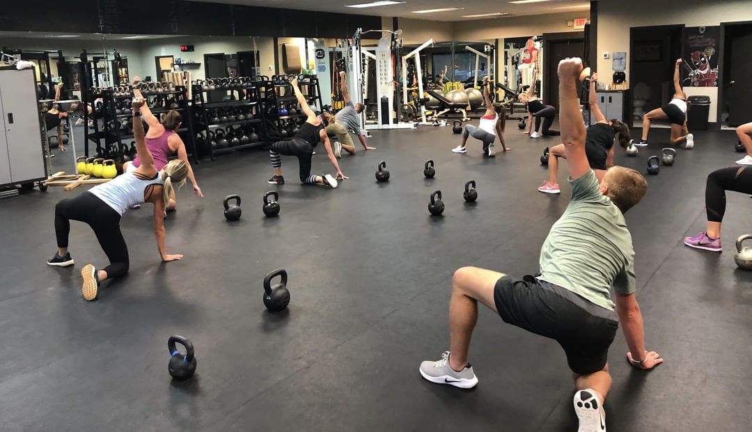 A group class holds half-kneeling stretches among rows of kettlebells.