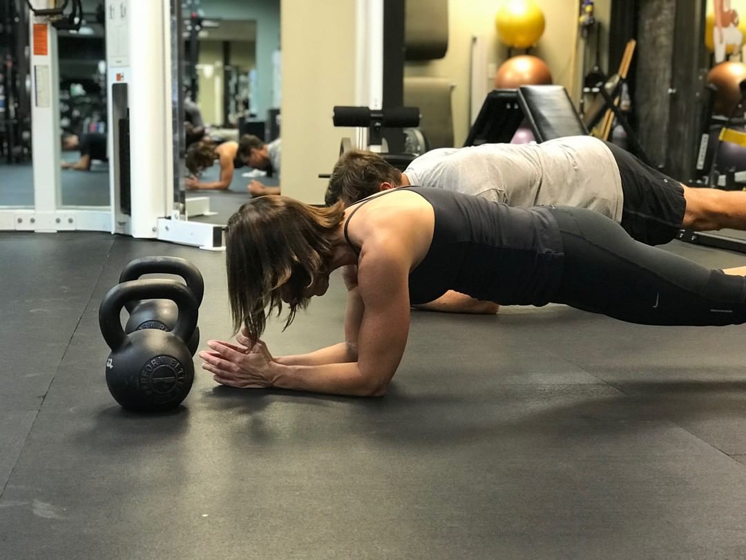 Members hold forearm planks beside their kettlebells.