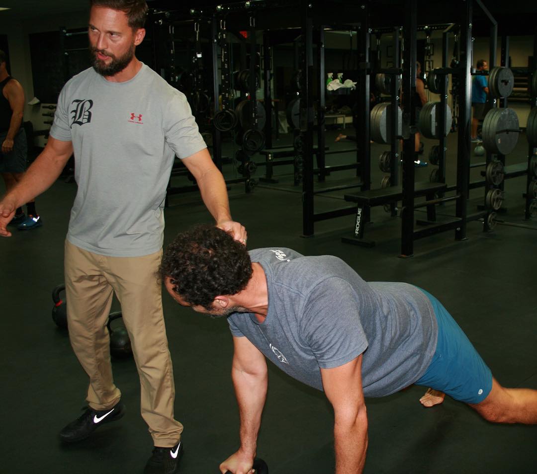 A coach cues a member during a kettlebell plank row.