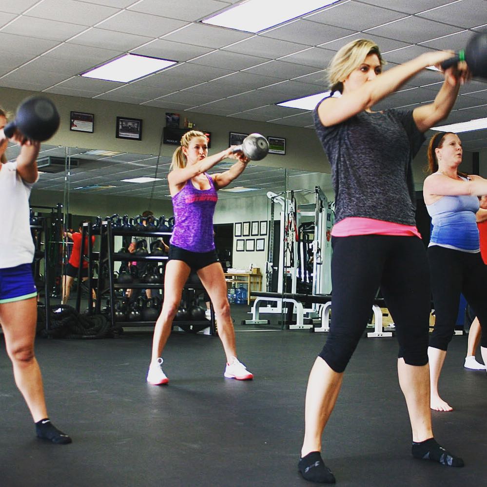 Members swing kettlebells together in a group class.
