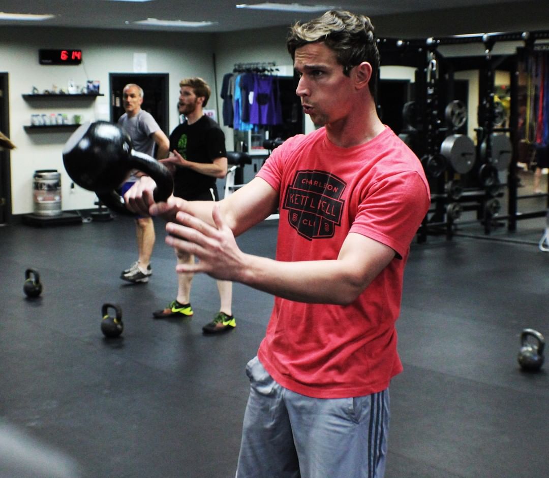 A member holds a kettlebell bottom-up while others train behind him.