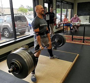 Pulling the bar past his knees on the platform while others watch.