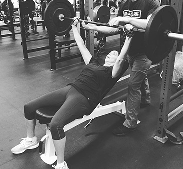 Pressing the bar from an incline bench with a coach spotting.